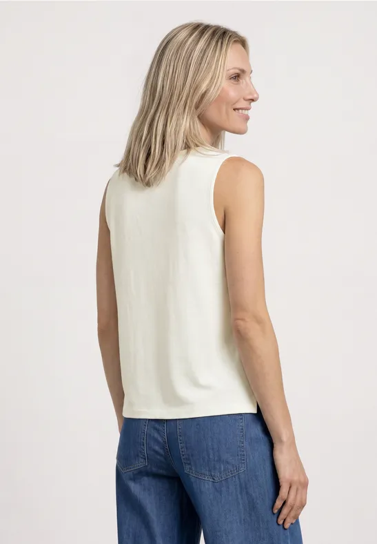 Een vrouw van achteren draagt een wit mouwloos shirt en blauwe spijkerbroek tegen lichte achtergrond.