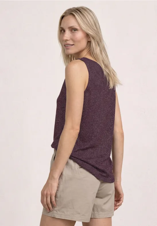 Een vrouw van achter, in een mouwloos paars topje en beige korte broek, tegen een lichte achtergrond.