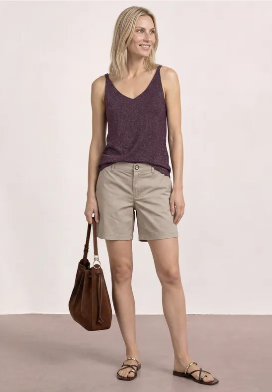 Vrouw in paarse top, beige shorts en sandalen, met een bruine tas.