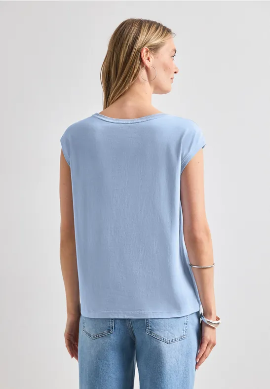 Eine Frau steht mit dem Rücken zur Kamera, trägt ein hellblaues T-Shirt und Jeans.