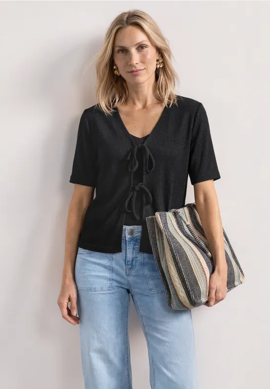 Frau mit blondem Haar trägt schwarzes Kurzarm-Oberteil, blaue Jeans und gestreifte Tasche.