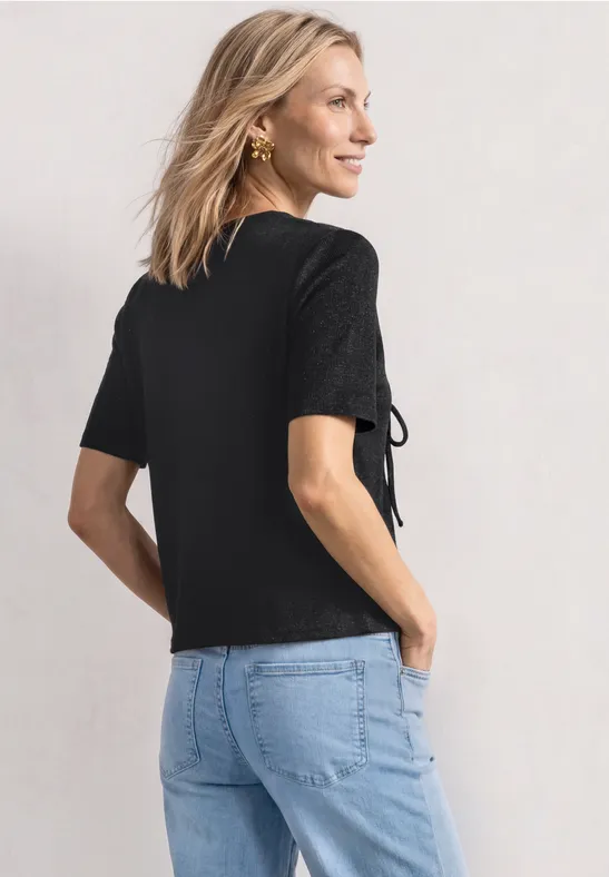 Frau von hinten in schwarzem Shirt mit Schnürung an den Ärmeln und Jeans