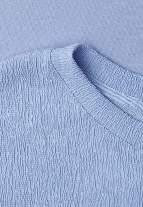 Nahaufnahme eines hellblauen Shirts mit strukturiertem Stoff und Rundhalsausschnitt.