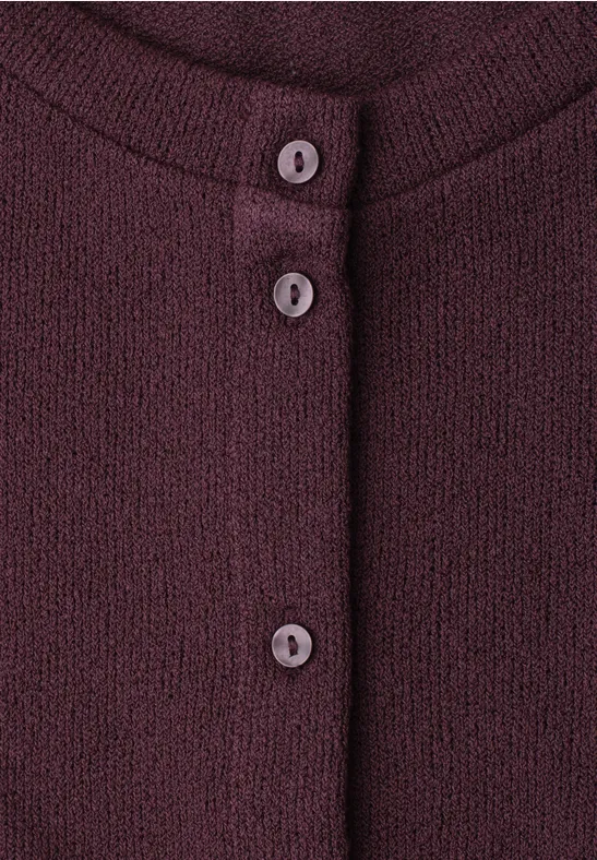 Close-up van een bordeauxrode gebreide cardigan met drie knopen aan de voorkant.