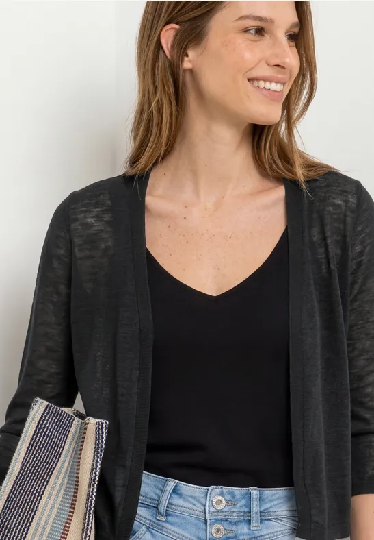 Vrouw met een zwarte top, dun vest, lichtblauwe jeans en een gestreepte tas.