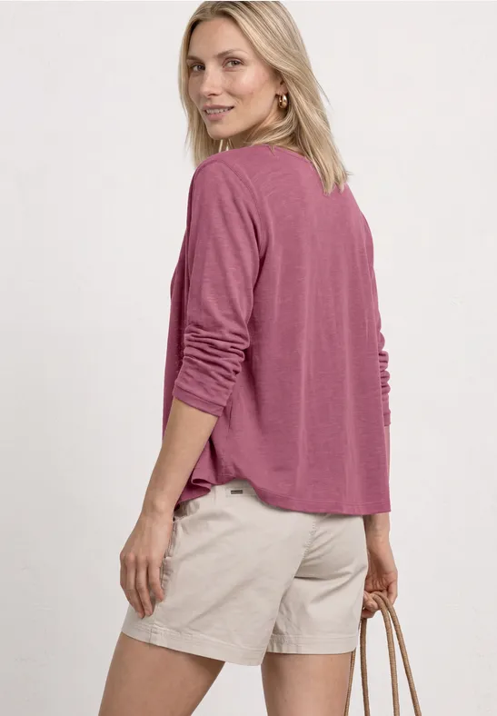 Frau von hinten in rosa Langarmshirt und beigen Shorts, die eine Tasche hält.