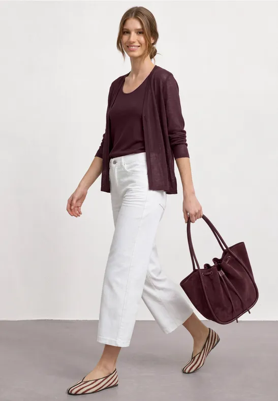 Frau in weinrotem Pullover, weißer Culotte, Zebra-Sandalen und passender großer Tasche.