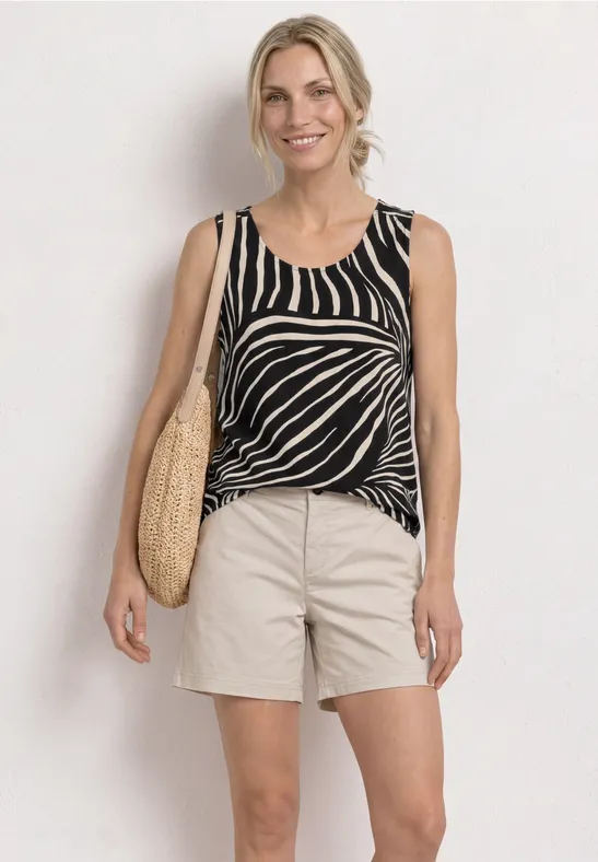 Vrouw in zebraprint top, beige short en strooien tas voor witte muur.