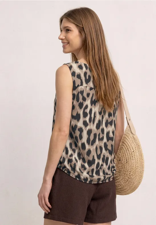 Une femme de dos porte un top léopard sans manches, des shorts bruns et un sac rond en paille.