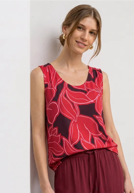 Vrouw in een rood mouwloos topje met groot bladvormig dessin en losse broek.