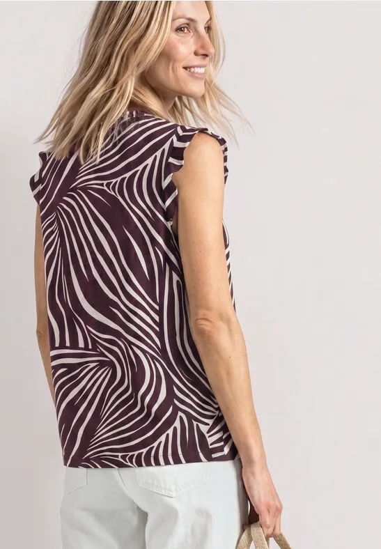 Vrouw van achteren in een mouwloos zebraprint top en een witte broek.