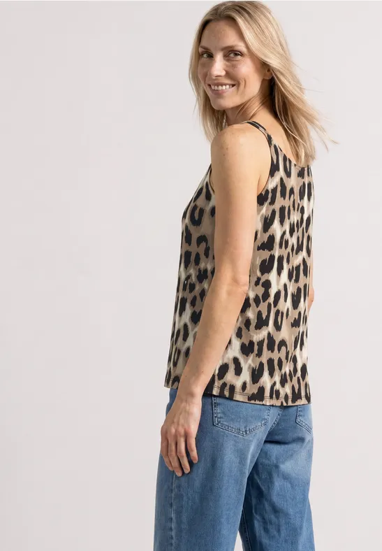 Vrouw in profiel draagt mouwloos luipaardtopje en blauwe jeans tegen lichte achtergrond.