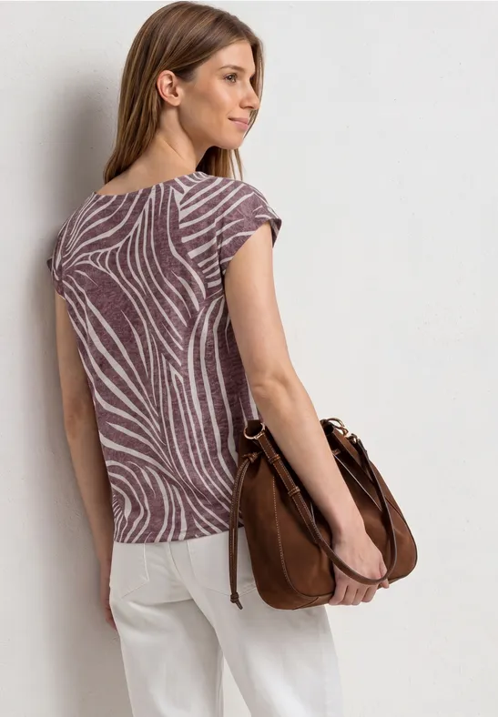 Frau von hinten in gemusterter Bluse und heller Hose, mit brauner Schultertasche.