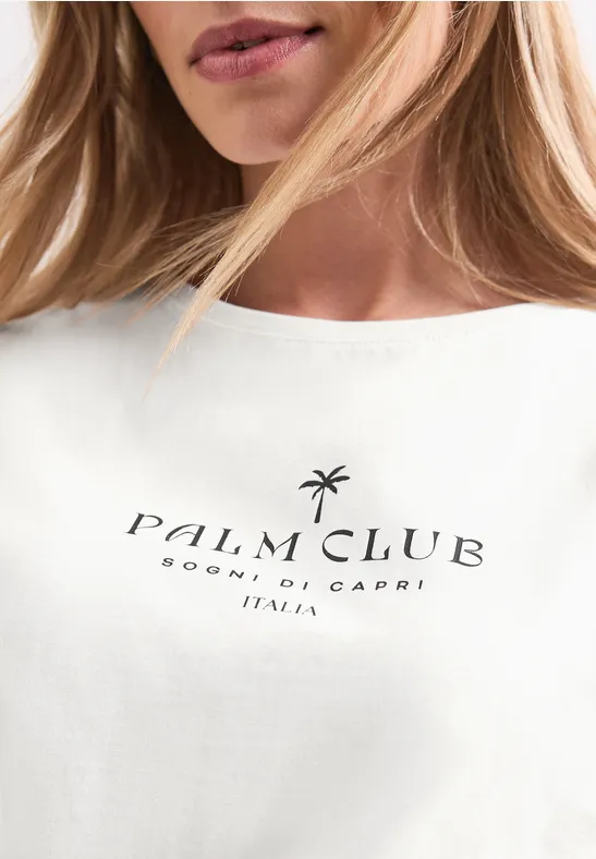 Close-up van een wit t-shirt met zwarte tekst ‘Palm Club Sorrento, Capri Italia’ en een palmboomlogo.