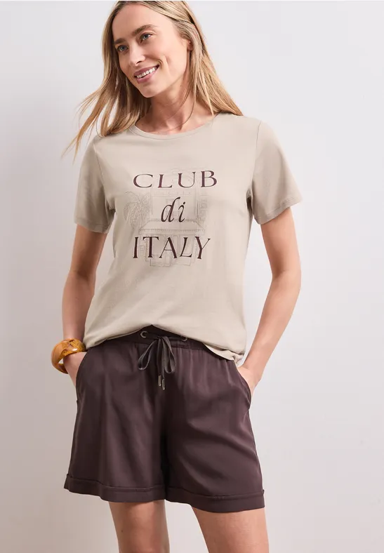 Vrouw met beige T-shirt 'CLUB di ITALY' en bruine leren short.