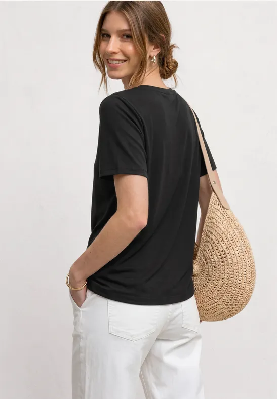 Vrouw van achteren in zwart t-shirt en witte broek met een gevlochten strooien tas.