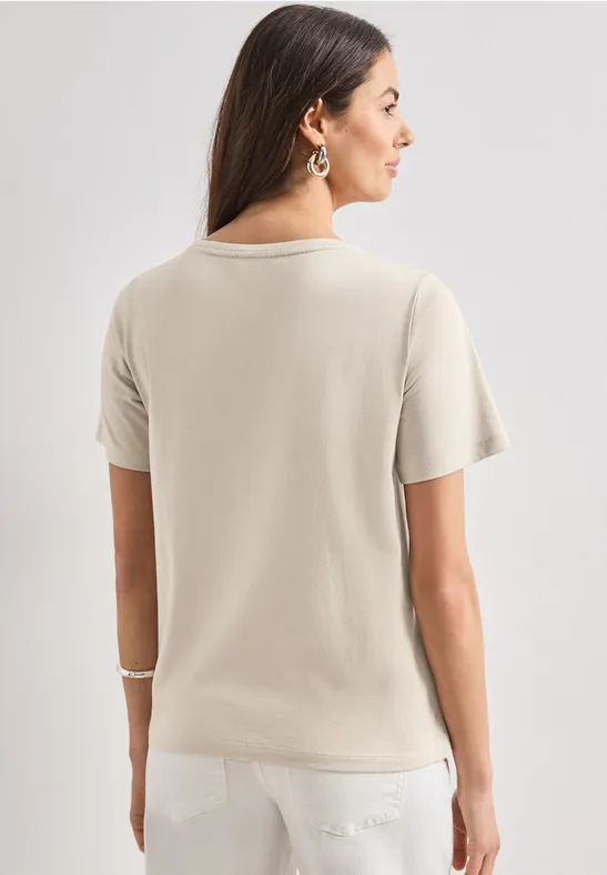 Frau von hinten in beigem T-Shirt und weißer Hose, mit dunklen, schulterlangen Haaren.