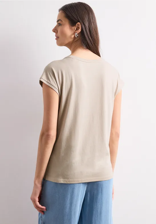 Frau von hinten in beigem T-Shirt mit kurzen Ärmeln und weitem Jeans, neutraler Hintergrund.
