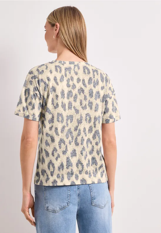 Vrouw van achteren in licht t-shirt met blauw-grijze luipaardprint en lichtblauwe jeans tegen witte achtergrond.