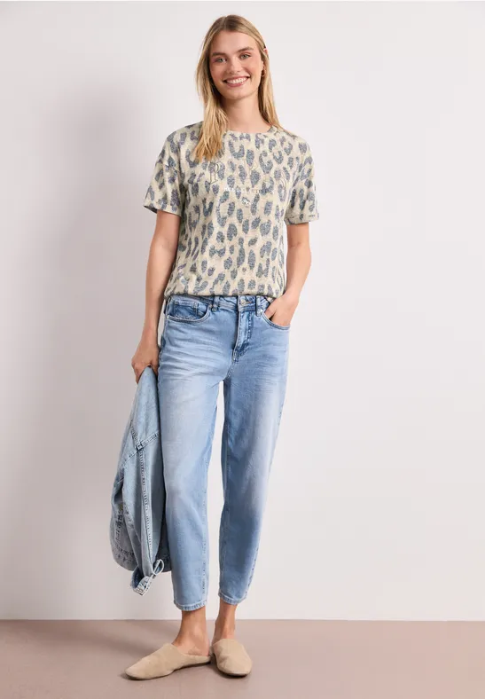 Vrouw in een shirt met print, lichte spijkerbroek en instappers, met een spijkerjack.