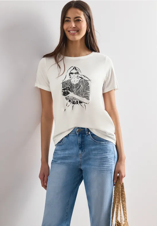 Frau in weißem T-Shirt mit Aufdruck, blauen Jeans und Schultertasche.