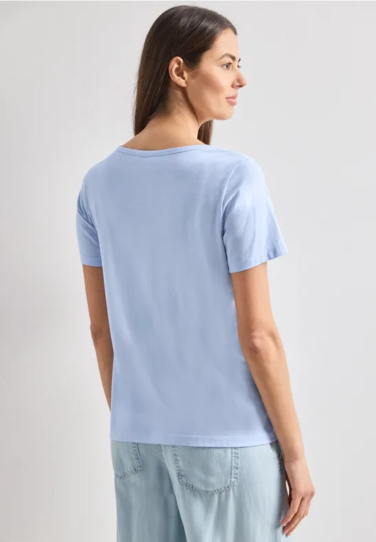 Een vrouw van achteren draagt een lichtblauw T-shirt en een spijkerbroek.