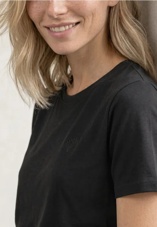 Portrait einer lächelnden Frau mit blonden Haaren in schwarzem T-Shirt vor hellem Hintergrund.