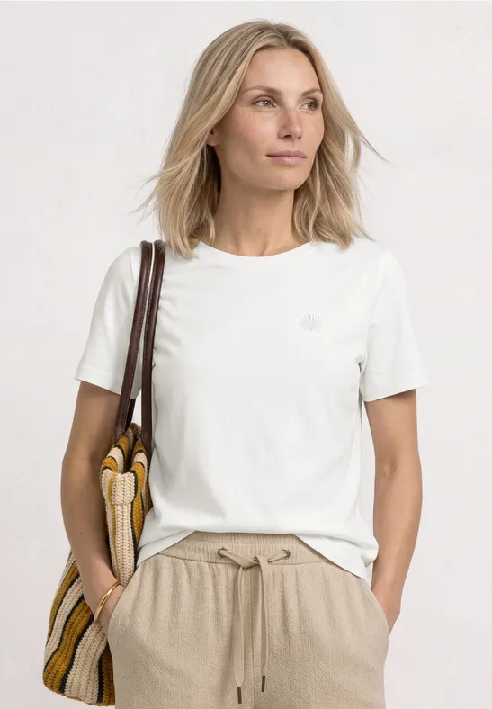 Jonge vrouw in wit T-shirt, beige broek en gestreepte handtas voor lichte achtergrond.