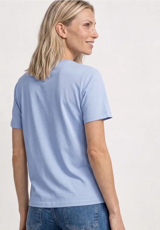 Rückansicht einer Person in hellblauem T-Shirt und Jeans, vor neutralem Hintergrund.