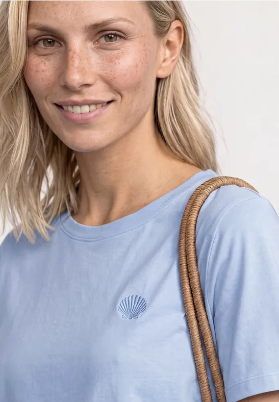 Frau trägt hellblaues T-Shirt mit kleinem Logo und Schultertasche.