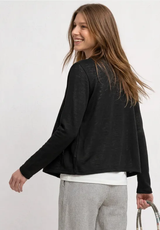 Vrouw van achteren in zwarte cardigan, wit shirt en grijze broek met handtas.