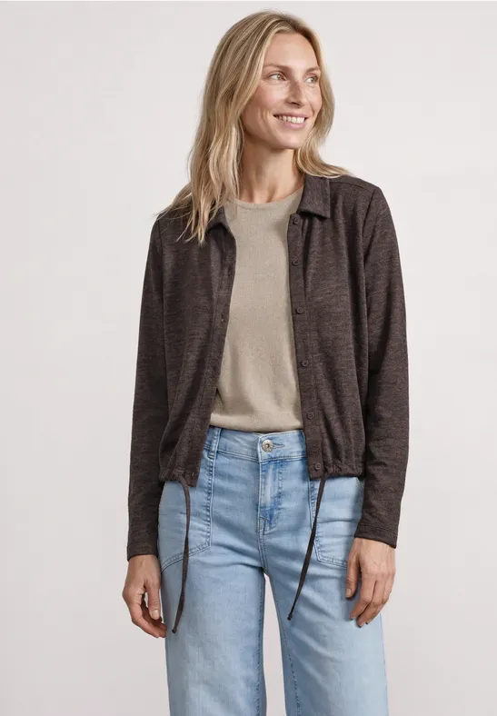 Femme portant une veste marron à carreaux, un t-shirt beige et un jean bleu sur fond blanc.