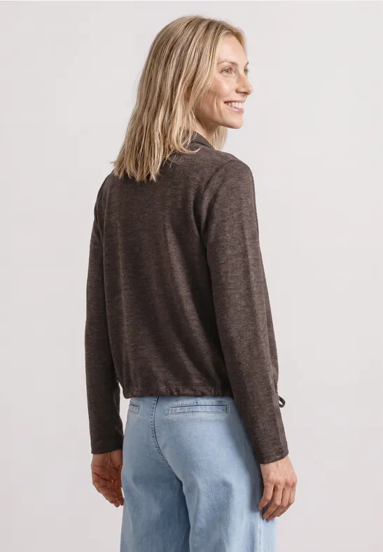 Femme de dos portant un pull marron foncé à manches longues et un jean bleu.
