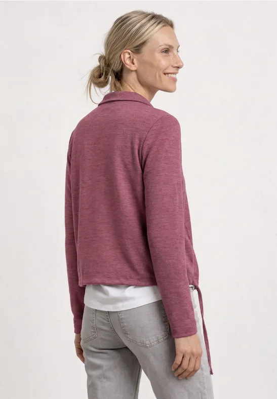 Frau von hinten in rosa Pullover, weißem Shirt und grauen Jeans, blonder Pferdeschwanz.