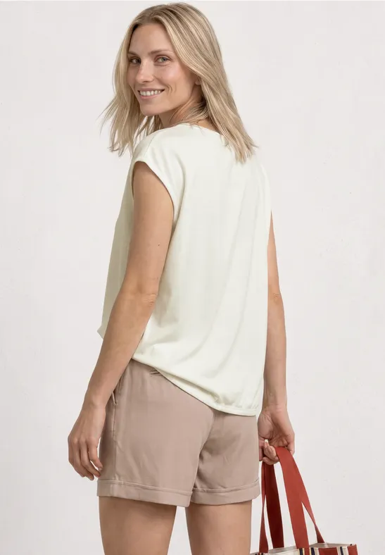 Frau von hinten in beigem Shirt und Shorts, trägt rote Tasche.