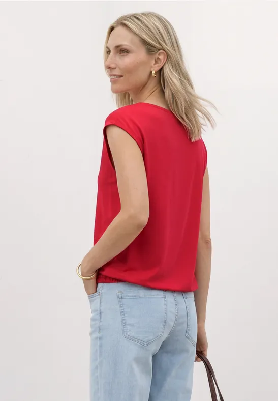 Vrouw van achteren met rood topje, lichte jeans en handtas.