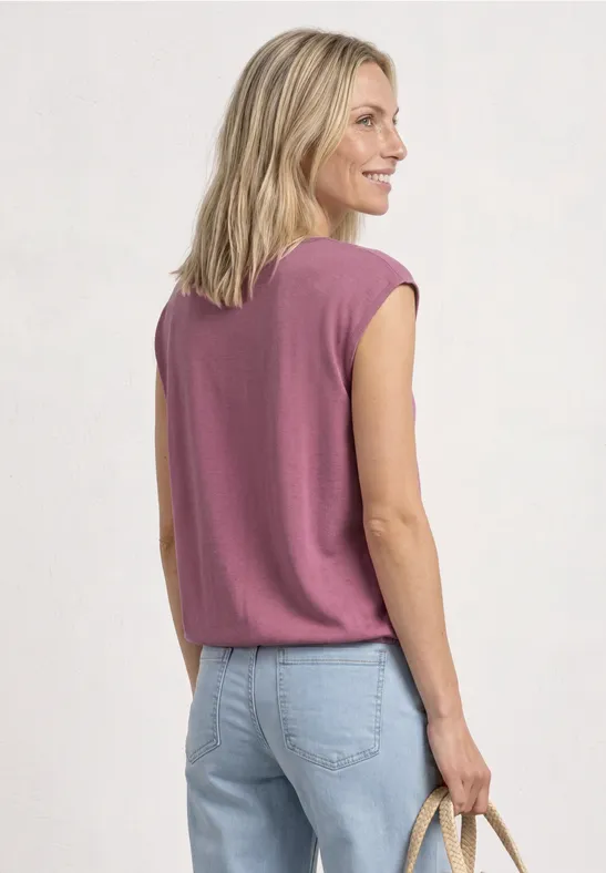 Rugaanzicht van een vrouw in een roze mouwloos shirt, lichtblauwe jeans en strozak.
