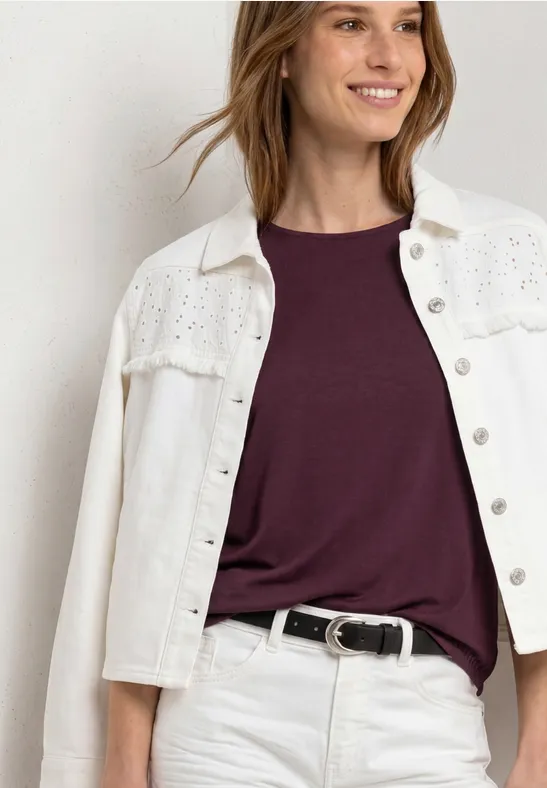 Oberkörperaufnahme einer Person in weißer Jeansjacke mit Stickerei, lila T-Shirt und schwarzem Gürtel.