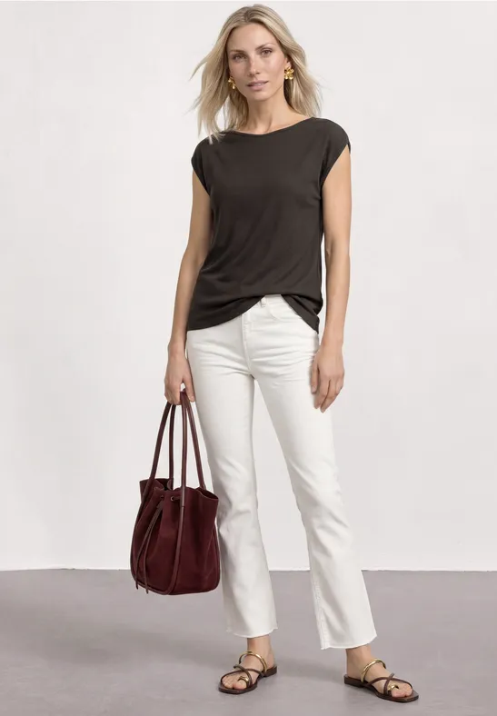 Femme portant un top noir, un pantalon blanc et des sandales, tenant un sac à main rouge.