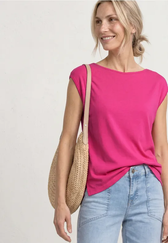 Une femme porte un top sans manches rose vif, un jean clair et un sac rond en paille.