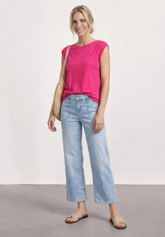 Femme en top rose, jean clair, sandales et sac beige.