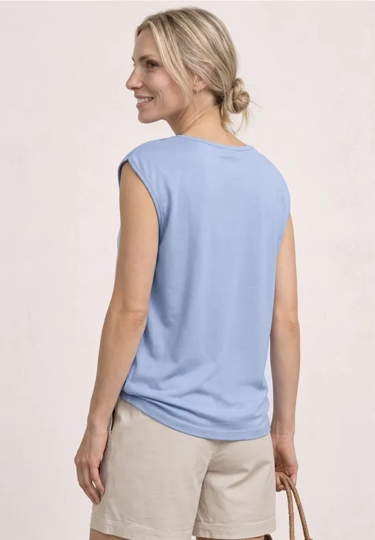 Vrouw van achteren met lichtblauw mouwloos shirt en beige short, ze draagt een gevlochten tas.