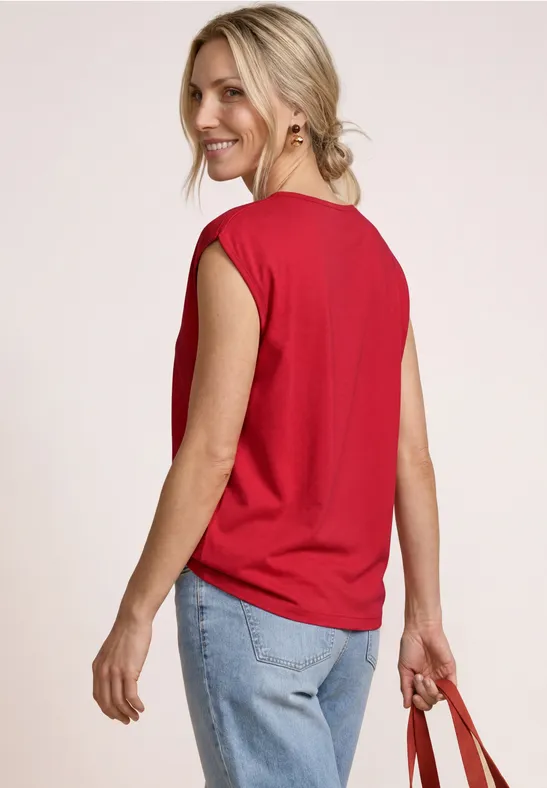 Frau von hinten in rotem, ärmellosem Shirt, hellblauen Jeans und roter Tasche.