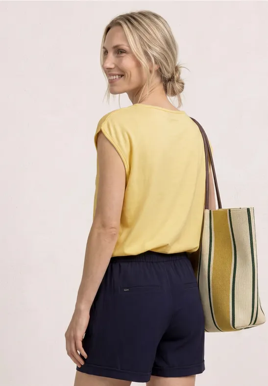 Vrouw van achteren in geel shirt, blond haar en donkere short, met gestreepte tas.