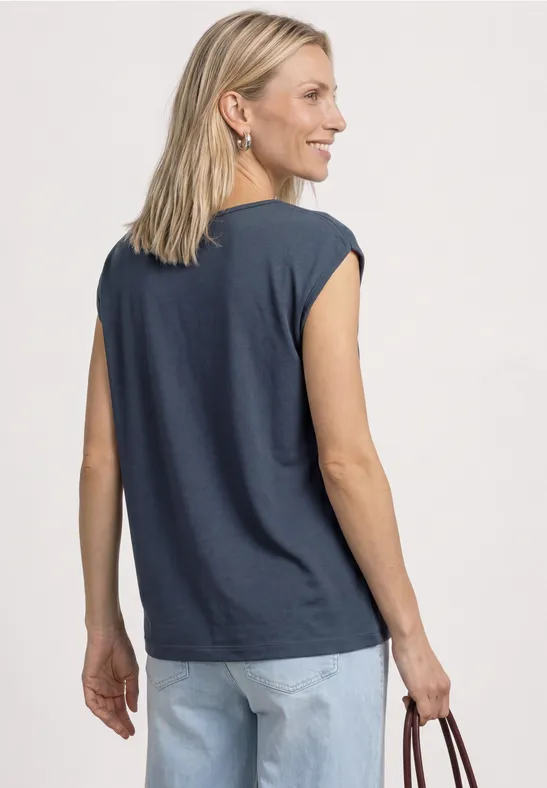 Vrouw van achteren in donkerblauwe mouwloze top, lichte jeans en met een handtas.