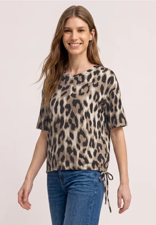 Frau trägt kurzärmliges Leopardenmuster-Top mit seitlichem Tunnelzug und blauen Jeans.