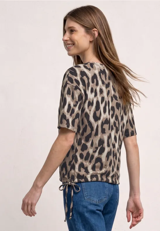 Frau in Jeans und kurzärmliger Bluse im Leopardenprint, Aufnahme in ¾-Ansicht von hinten.