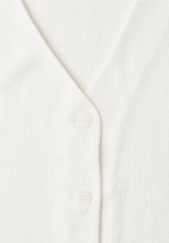 Close-up van een wit gebreid vest met V-hals en twee knopen.