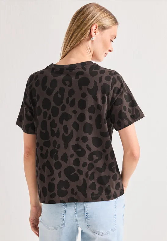 Rückenansicht einer Frau in hellen Jeans und kurzärmligem T-Shirt mit dunklem Leopardenmuster.
