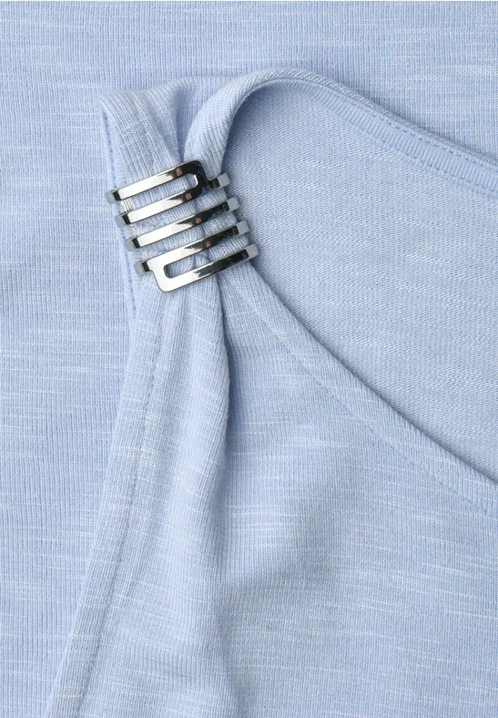 Nahaufnahme eines hellblauen Stoffs mit vier silbernen Schnallen an einem Träger.